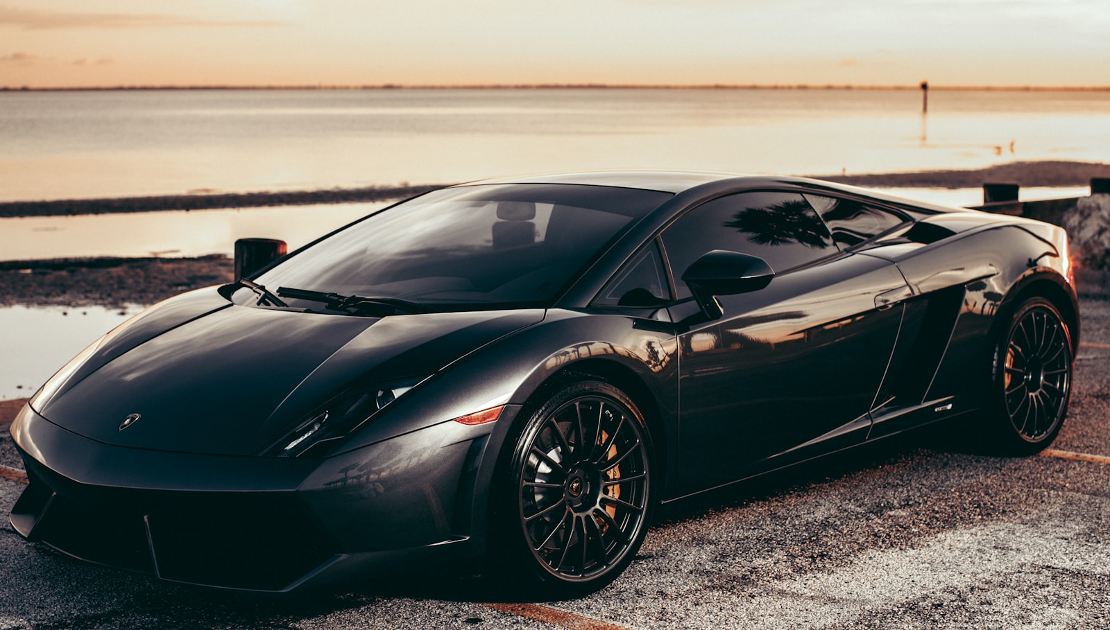 Black Lamborghini Gallardo by the sea at sunset