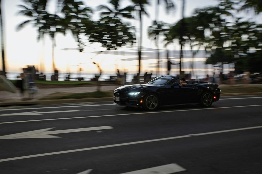 Black convertible driving on a coastal road at dusk